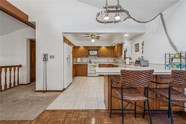 kitchen featuring white appliances, light countertops, a tray ceiling, a peninsula, and brown cabinetry