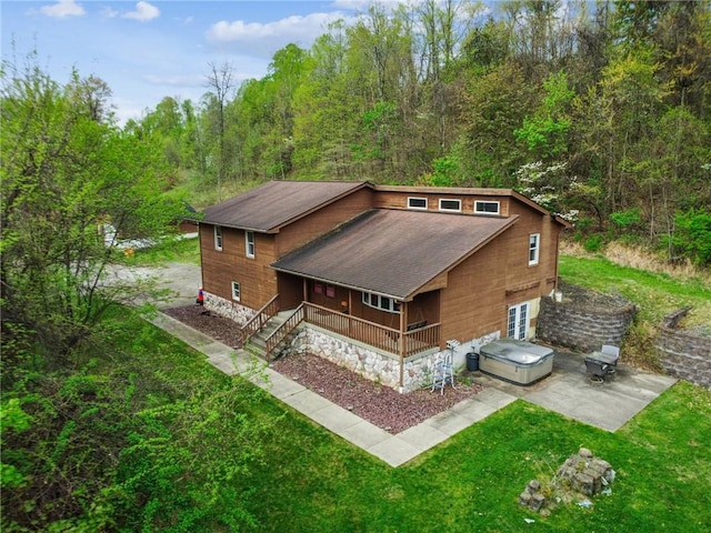 back of property with a porch, a lawn, a shingled roof, and a view of trees