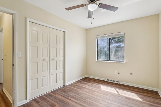 unfurnished bedroom featuring visible vents, a closet, wood finished floors, baseboards, and a ceiling fan
