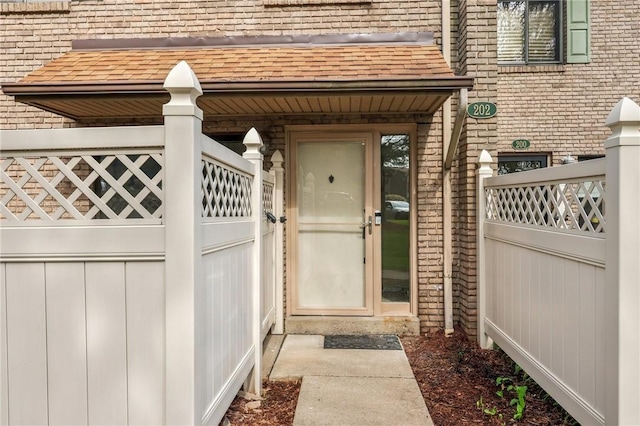 view of exterior entry featuring brick siding and a shingled roof