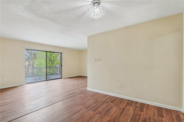spare room featuring baseboards, wood finished floors, and a chandelier