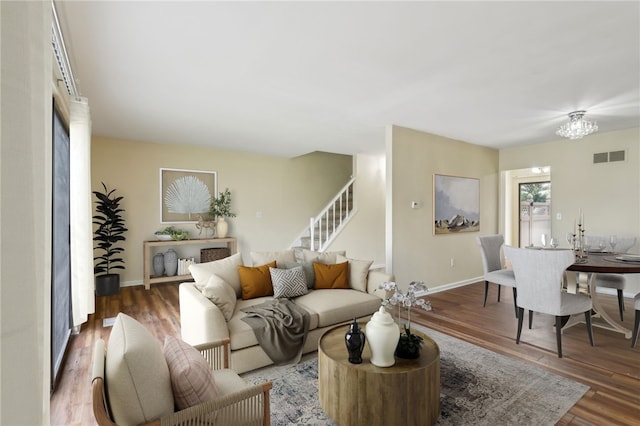 living room featuring visible vents, wood finished floors, baseboards, stairway, and a notable chandelier