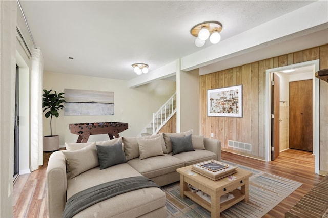 living area with wooden walls, stairway, wood finished floors, and visible vents