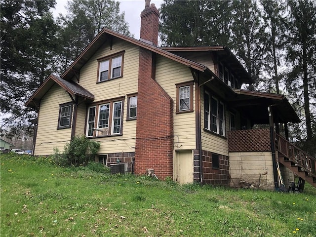 view of property exterior featuring a chimney, stairway, central AC, and a lawn