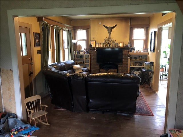 living room with a wealth of natural light, wood-type flooring, and a brick fireplace