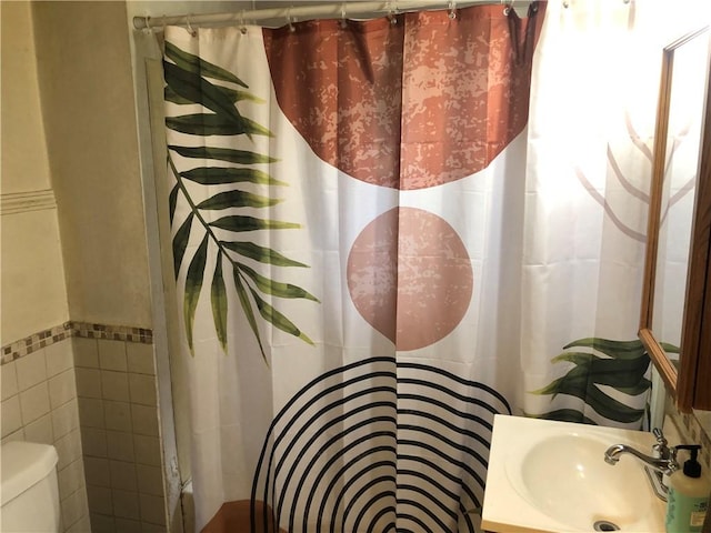 full bathroom with tile walls, a shower with shower curtain, toilet, and a sink