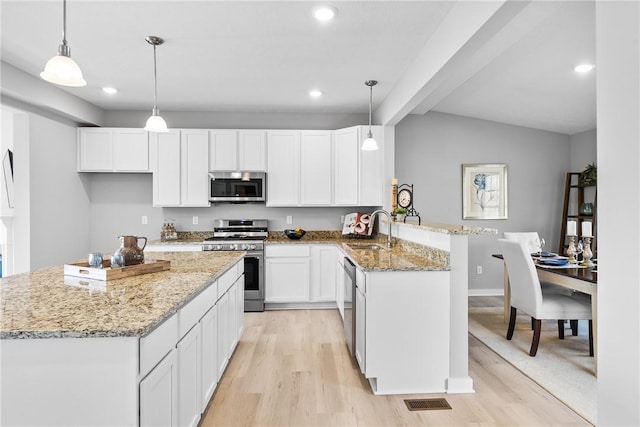 kitchen featuring light wood-style flooring, stainless steel appliances, white cabinets, a sink, and a peninsula