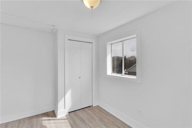 unfurnished bedroom with baseboards, light wood-style flooring, and a closet