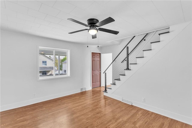 interior space featuring stairway, a ceiling fan, visible vents, baseboards, and wood finished floors