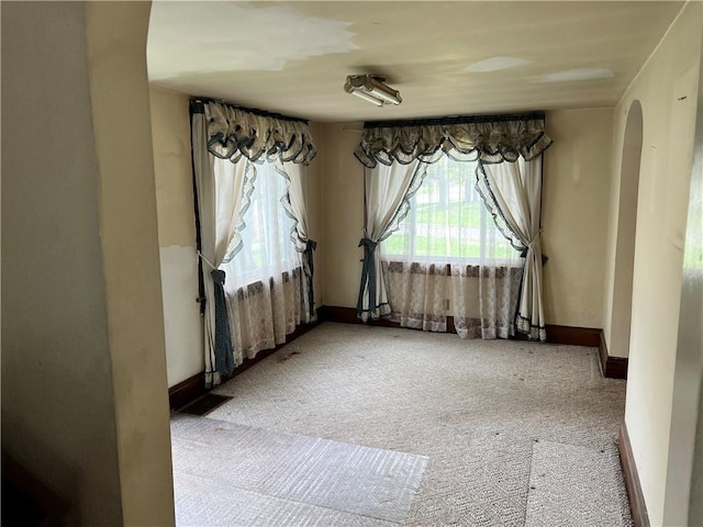unfurnished room with carpet, baseboards, and arched walkways