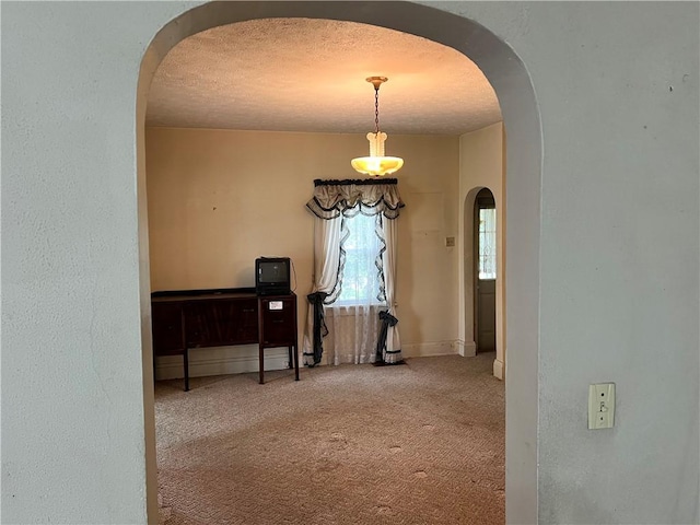 hallway with arched walkways, carpet flooring, a textured ceiling, and baseboards
