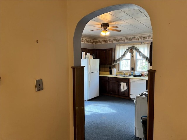 kitchen featuring dark carpet, dark brown cabinets, arched walkways, white appliances, and a ceiling fan