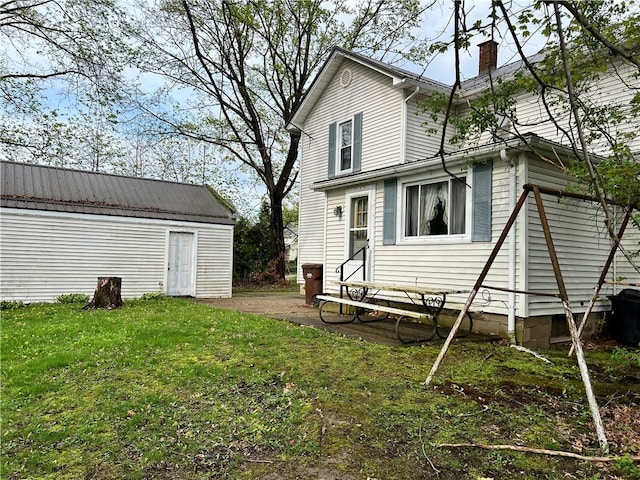 rear view of property with a chimney, an outbuilding, and a lawn