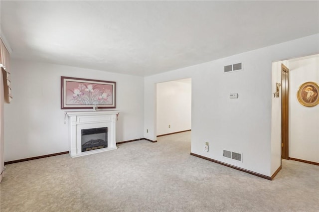 unfurnished living room with visible vents, light carpet, and a glass covered fireplace