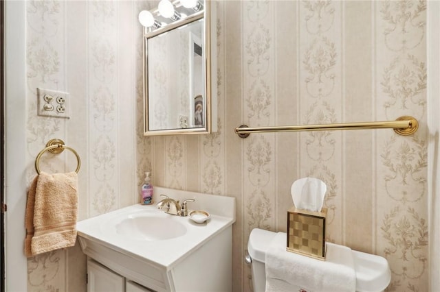 bathroom featuring toilet, wallpapered walls, and vanity