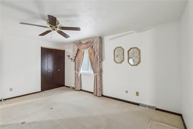 carpeted spare room featuring a ceiling fan, visible vents, and baseboards