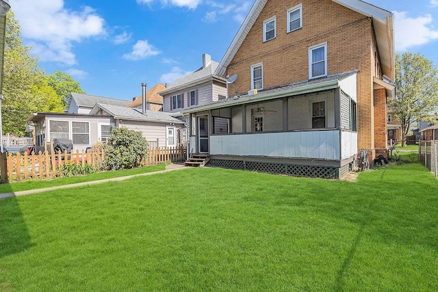 back of house with brick siding, a yard, a fenced backyard, and a sunroom