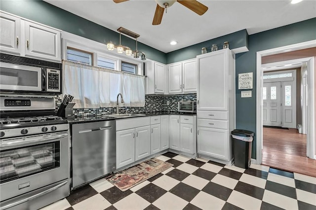 kitchen with a sink, a ceiling fan, dark floors, dark countertops, and appliances with stainless steel finishes