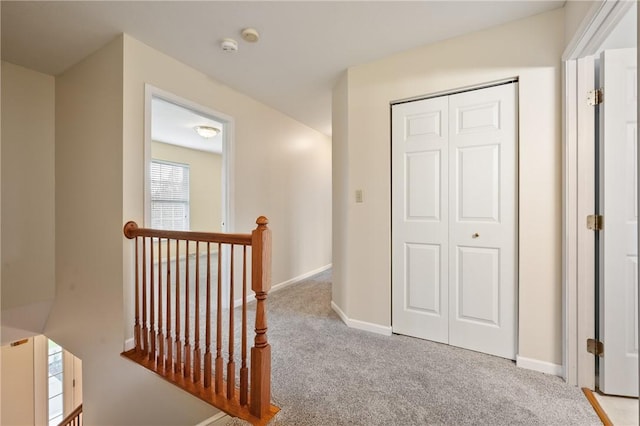 hall with an upstairs landing, carpet floors, and baseboards