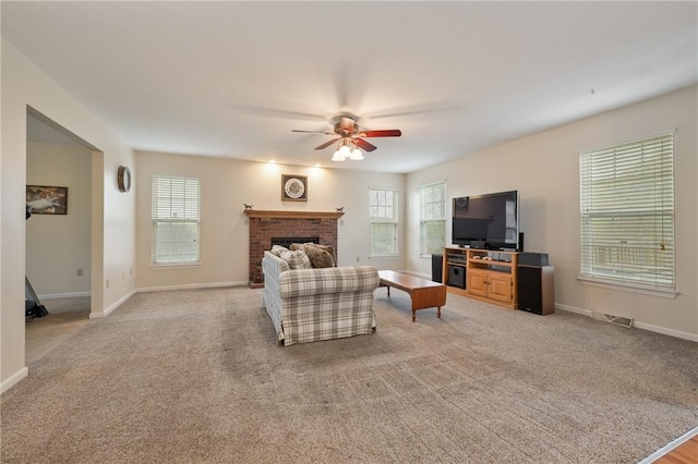 living room with a brick fireplace, a ceiling fan, light carpet, and baseboards