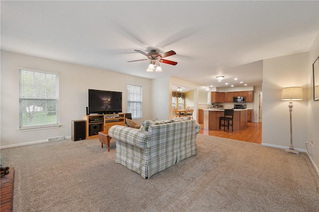 living room featuring a ceiling fan, baseboards, light carpet, and plenty of natural light