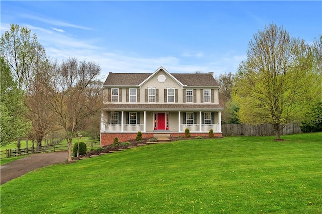 colonial-style house with aphalt driveway, a front lawn, covered porch, and fence