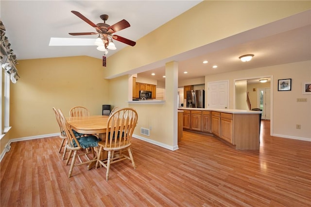 dining area with vaulted ceiling with skylight, light wood-style floors, ceiling fan, visible vents, and baseboards