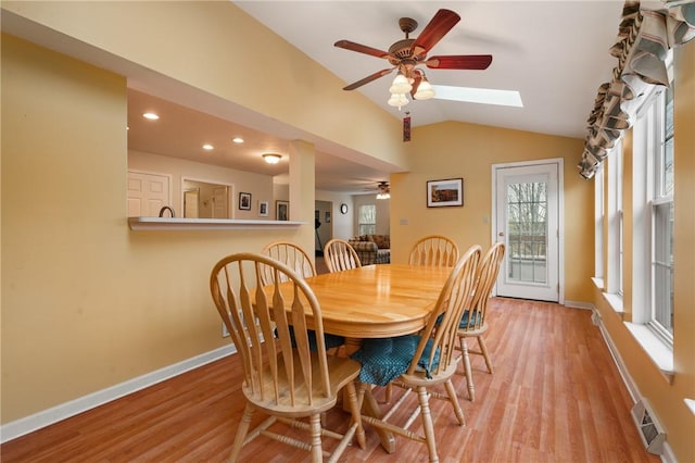 dining room with vaulted ceiling with skylight, ceiling fan, light wood-style floors, visible vents, and baseboards