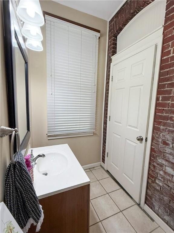 bathroom featuring tile patterned flooring, baseboards, vanity, and brick wall