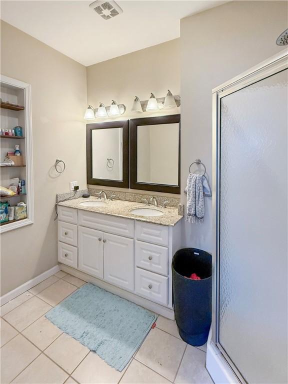 bathroom with a stall shower, tile patterned flooring, double vanity, and a sink