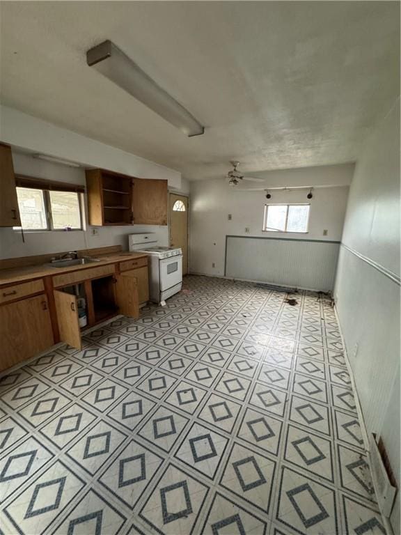 kitchen with white gas range oven, brown cabinets, open shelves, a sink, and ceiling fan