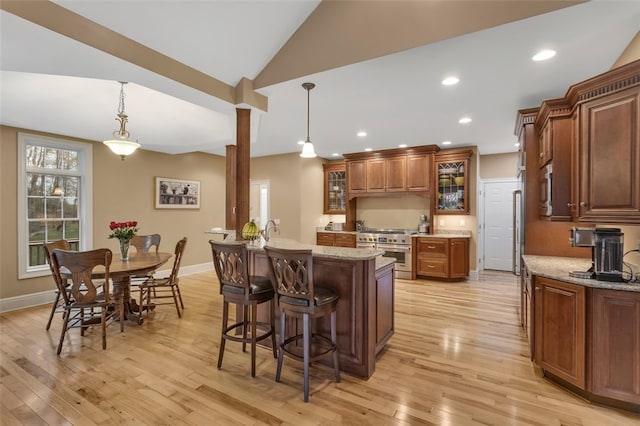 kitchen with light wood-style floors, glass insert cabinets, decorative columns, a breakfast bar, and high quality appliances