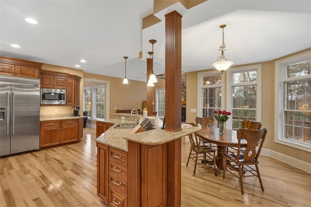 kitchen with brown cabinets, light wood-style flooring, a sink, built in appliances, and ornate columns