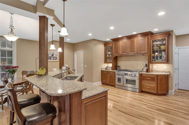 kitchen featuring brown cabinets, a sink, light wood-style floors, range with two ovens, and a kitchen bar