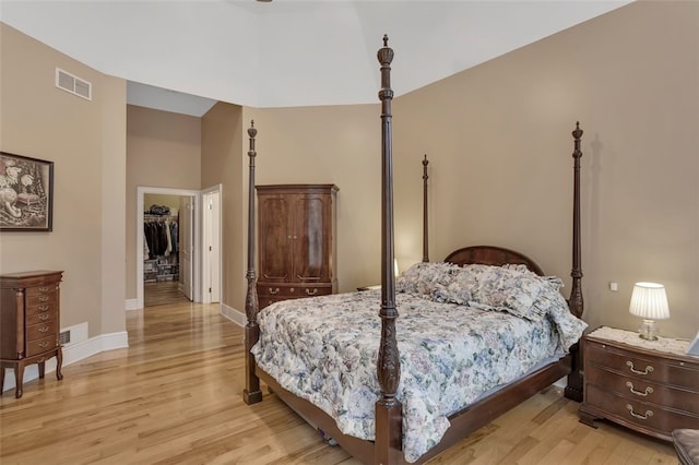 bedroom with visible vents, light wood-type flooring, a walk in closet, and baseboards