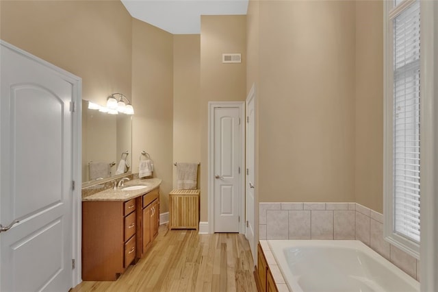 full bathroom with wood finished floors, a bath, vanity, visible vents, and a high ceiling
