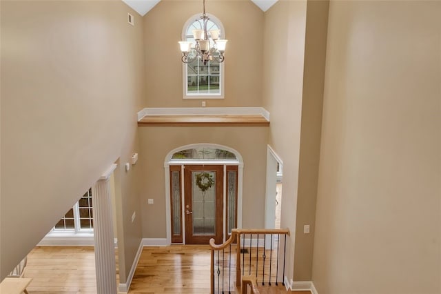 foyer entrance featuring wood-type flooring, an inviting chandelier, high vaulted ceiling, and visible vents