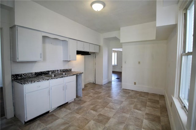 kitchen with baseboards, white cabinets, stone finish floor, and a sink