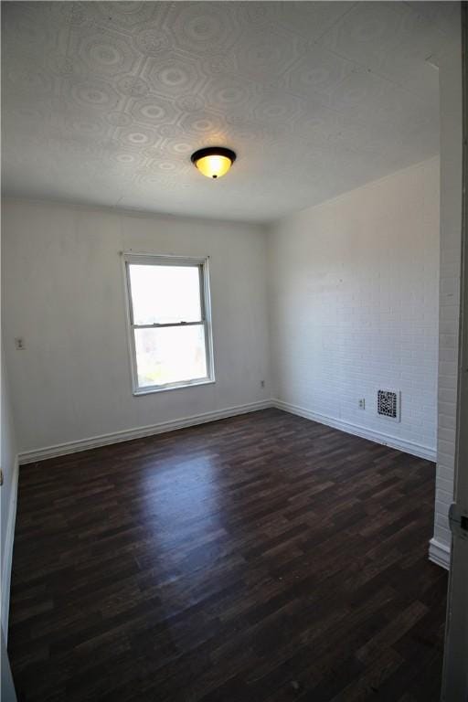 empty room featuring visible vents, dark wood-style floors, and baseboards