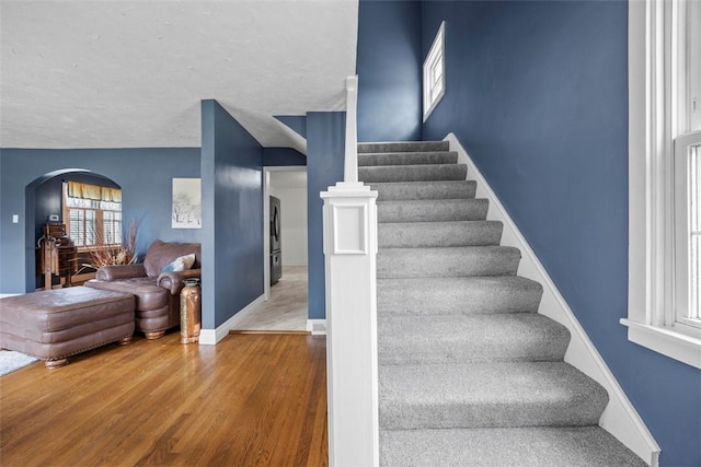 stairs with wood finished floors, baseboards, and arched walkways