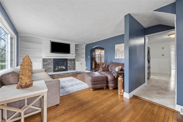living area featuring a wainscoted wall, arched walkways, a fireplace, wood finished floors, and built in features