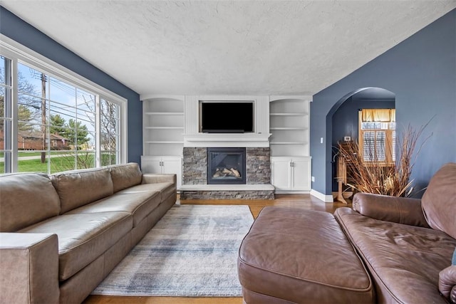 living area with arched walkways, a textured ceiling, wood finished floors, and plenty of natural light