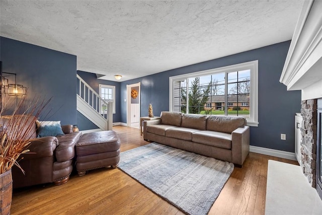 living area featuring stairway, a fireplace, wood-type flooring, baseboards, and a textured ceiling