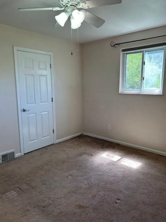carpeted spare room featuring baseboards, visible vents, and ceiling fan