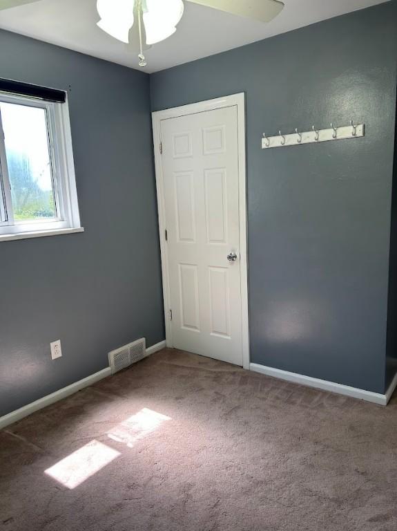 empty room with baseboards, visible vents, a ceiling fan, and carpet