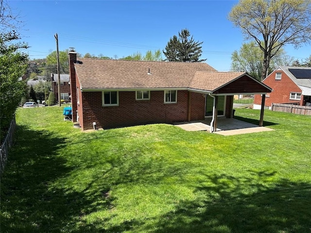rear view of property featuring brick siding, a patio area, a lawn, a chimney, and fence
