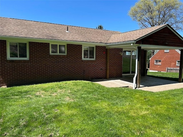 rear view of house with a lawn, brick siding, a shingled roof, and a patio area