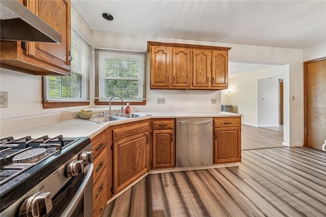 kitchen with stainless steel appliances, under cabinet range hood, light countertops, a sink, and light wood-type flooring