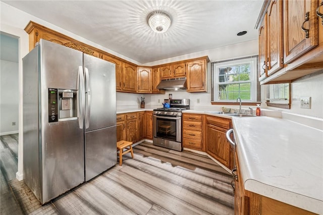 kitchen featuring light wood-style flooring, brown cabinetry, stainless steel appliances, under cabinet range hood, and a sink