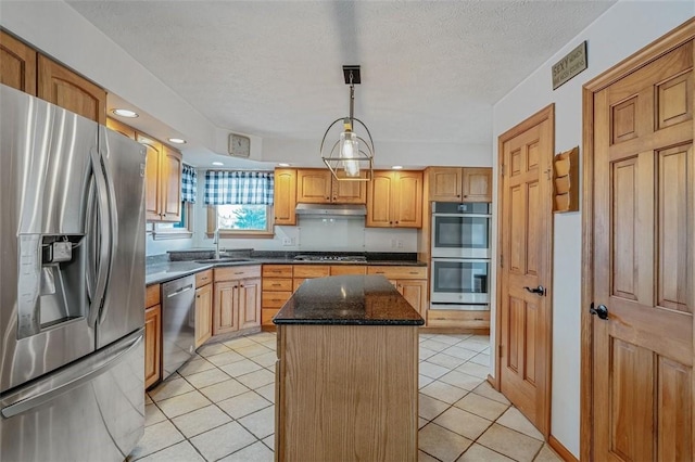 kitchen with a sink, stainless steel appliances, under cabinet range hood, light tile patterned flooring, and a kitchen island